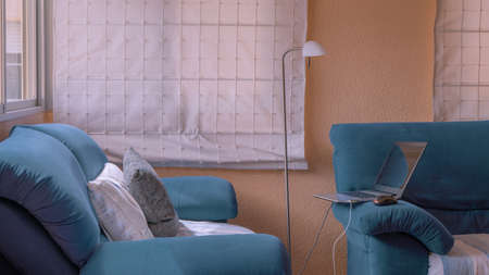 Comfortable, cozy, bright living room with a laptop, white curtains, window, minimalist lamp, blue sofaの写真素材