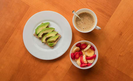 Avocado toast, cup of coffee and strawberry-banana mix in a wooden tableの写真素材