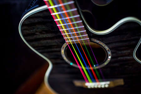 electric acoustic unplugged black guitar with colorful rainbow strings dark backgroundの写真素材