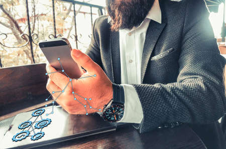 youn adult rich businessman with beard and smartwatch using his pro tablet and his smartphone holographic futuristic web and economy iconsの写真素材