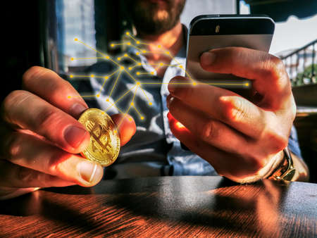 bitcoin holding rich male using his phone for remote exchange e-commerce e-business on the pub tableの写真素材