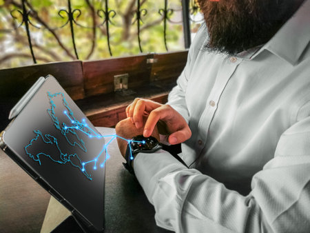 bearded adult rich businessman touching economy touching his smart watch and connecting to his pro tablet and internet world map holographicの写真素材