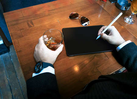 top view businessman with smart watch holding whiskey glass and tablet pencil with his blank screen pro tablet on the tableの写真素材