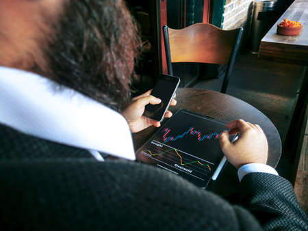 business man with beard who has smart watch using pro tablet and pencil interacting with tablet screen and smart phone checking for-ex stock exchange data on the mobile screensの写真素材