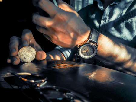 young adult male with sunglasses and watch using his smartphone and flipping bitcoin on the tableの写真素材