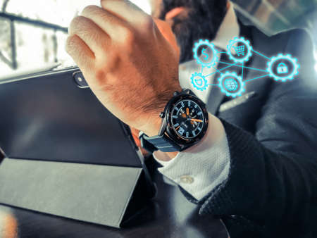 bearded adult rich businessman who has smart watch using his pro tablet and work remotely holographic economy online technological icons floatingの写真素材