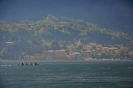 View of Lake Como on a cloudy day with rowers in the foreground in Bellagio, a charming tourist village between the lake and the mountains of the Alps. Located in the Lombardy region, northern Italyの写真素材