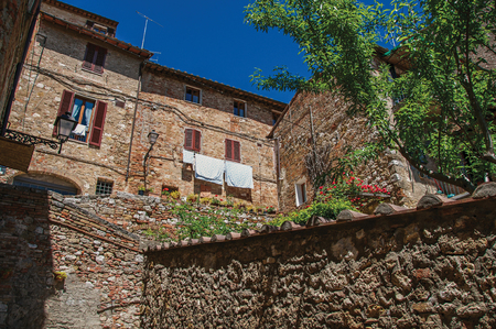 View of stone wall, old buildings with flowering plants and blue sky at Colle di Val d'Elsa. The village with its historic center preserved and known by its crystal production. In the Tuscany regionの写真素材