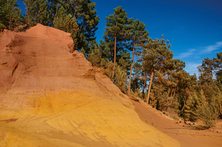View of ocher land, trees under a sunny blue sky, in the park Sentiers des Ocres, near the village...