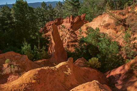 View of ocher land, trees under a sunny blue sky, in the park Sentiers des Ocres, near the village...