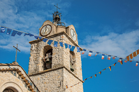 Close-up of church steeple on stone bricks at sunset, with clock and flags, in the lovely village of Greoux-les-Bains. In Alpes-de-Haute-Provence department, Provence region, southeastern Franceの写真素材