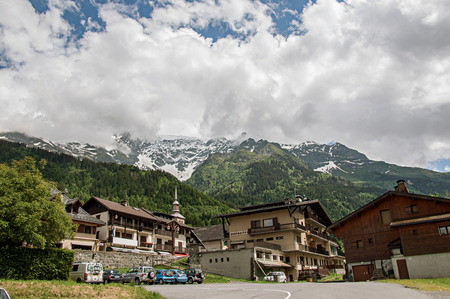 Houses and bellow tower in front of snowy mountains in the sunny day at Les-Contamines-Montjoie. A small alpine village located in the Haute-Savoie Province, near the Mont Blanc in the French Alps.のeditorial素材