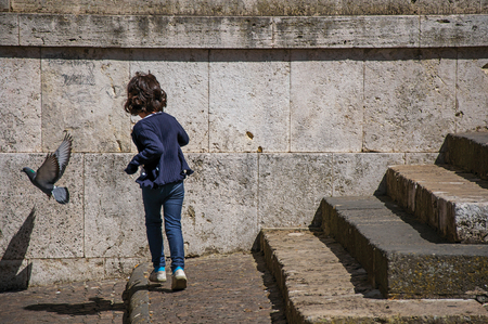 Orvieto, Italy - May 17, 2013. View of little girl playing with dove near stone staircase in Orvieto, a pleasant and well preserved medieval city. Located in Umbriaのeditorial素材