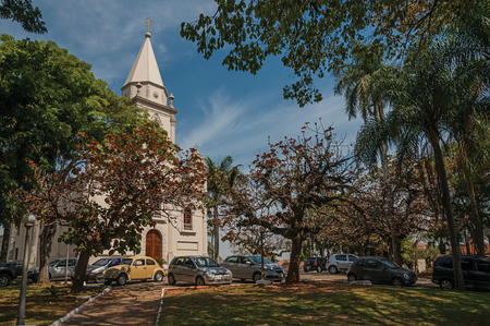 Sao Manuel, southeast Brazil - September 09, 2017. Church facade with parked cars and evergreen garden in the sunny day at San Manuel. A cute little town in the countryside of São Paulo State.のeditorial素材