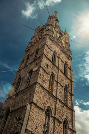 Stone gothic tower with golden clock and shinny sky in Ghentの写真素材