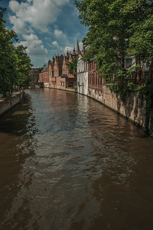 Wooded gardens and brick buildings on the canal's edge in the sunny day at Bruges. With many canals and old buildings . Northwestern Belgium.の写真素材