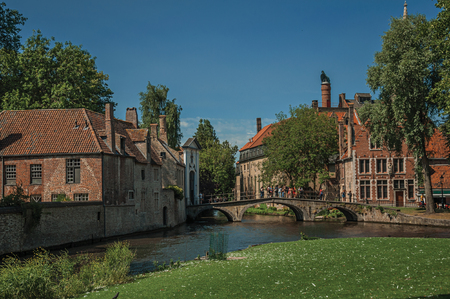 Old brick buildings next to the canal and bridge with people in the sunny day at Bruges.の写真素材