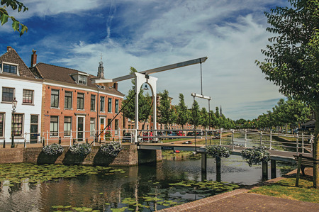 Canal with street on the banks, brick houses and bascule bridge on a sunny day in Weesp. Quiet and pleasant village full of canals and green near Amsterdamのeditorial素材