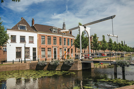 Canal with street on the banks, brick houses and bascule bridge on a sunny day in Weesp. Quiet and pleasant village full of canals and green near Amsterdamのeditorial素材