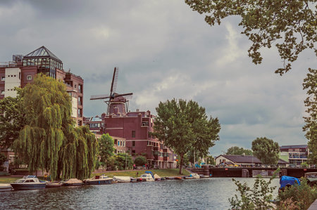 Big wooded canal with brick buildings, moored boats and cloudy sky in Amsterdam. Famous for its huge...