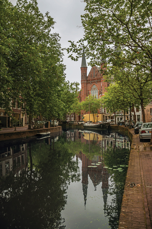 Canal with trees along, brick church and cloudy sky, in the city center of Gouda. Very popular day trip destination, is famous for its tasty Gouda cheese.のeditorial素材