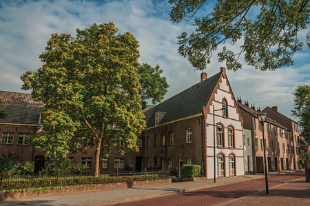 Empty street with large brick house, trees in a garden surrounded by fence and blue sky at sunset in s-Hertogenbosch. Gracious historical city with vibrant cultural life. Southern Netherlands.の写真素材