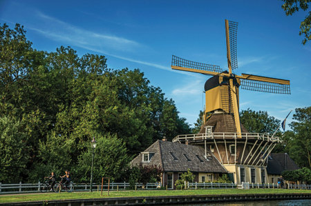 Weesp, northern Netherlands - June 26, 2017. Cyclist and wooden yellow windmill next to wide...