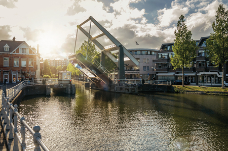 Weesp, northern Netherlands - June 26, 2017. Tree-lined wide canal with houses and lifted bascule bridge on sunset in Weesp. Quiet and pleasant village full of canals and green near Amsterdam.のeditorial素材
