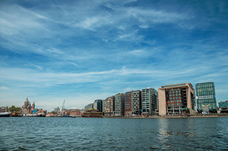 Amsterdam, northern Netherlands - June 27, 2017. Port, church towers and modern buildings on canal bank and blue sky in Amsterdam. Famous for its huge cultural activity, graceful canals and bridges.のeditorial素材