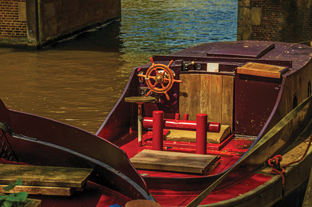Wooden steering wheel on poop deck of boat moored on the canal side in Amsterdam. The city is famous for its huge cultural activity, graceful canals and bridges. Northern Netherlands. Retouched photo.の写真素材
