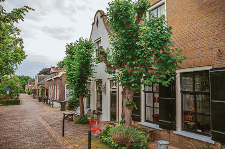 Charming and quiet street with brick rustic houses and greenery in cloudy day at Drimmelen. A lovely small hamlet with harbor and elegance streets. Southern Netherlands.の写真素材