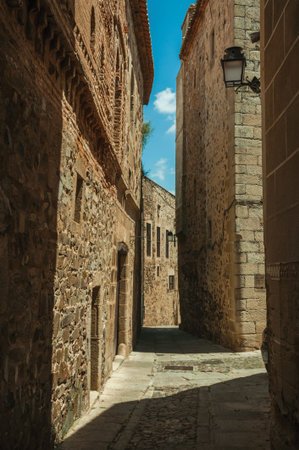 Narrow alley with old stone buildings and public lamp stuck in the wall, in a sunny day at Caceres....