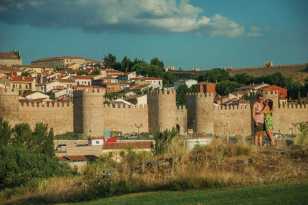 Avila, Spain - July 22, 2018. Couple of lovers over hill and wall with towers around Avila in the background. It has the longest and imposing wall completely encircling this well-kept gothic town.のeditorial素材
