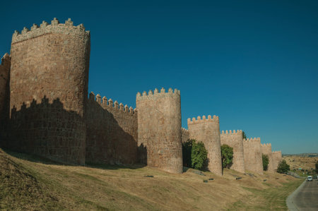 Lined stone towers on the large city wall in Romanesque style next to street, in a sunny day at...