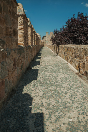 Pathway over thick stone wall with battlement and merlons around the town, in a sunny day at Avila. It has the longest and imposing wall completely encircling this well-kept gothic town of Spain.の写真素材