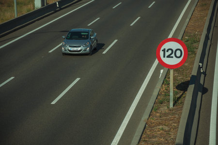 Lonely grey car passing through multi lane highway and SPEED LIMIT signpost, on sunset in Madrid....