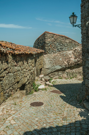 Charming facade of old houses and stone wall with big round rock, in deserted alley on slope in a sunny day at Monsanto. Considered one of the cutest and most peculiar historic village of Portugal.の写真素材