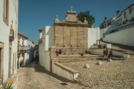 Charming water fountain made of stone in baroque style in between two cobblestone alleys, in a sunny...