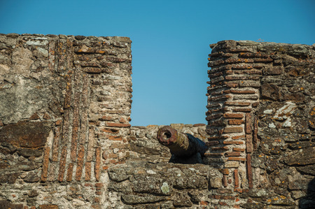 Close-up of old rusty iron cannon aiming through crenel in the stone outer wall, in a sunny day at Marvao. An amazing medieval fortified village perched on a granite crag in eastern Portugal.の写真素材