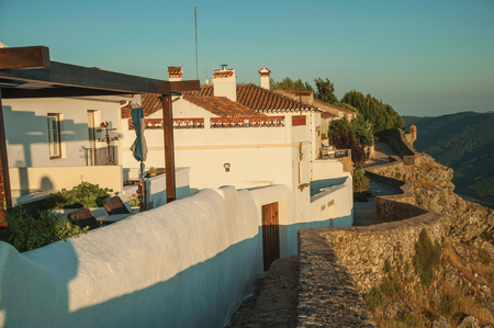 Stone wall and white old houses over rocky cliff, with hilly landscape covered by trees on sundown at Marvao. An amazing medieval fortified village perched on a granite crag in eastern Portugal.の写真素材