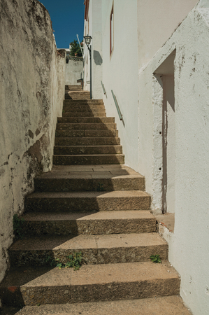 Worn whitewashed wall and pathway made of stone with stairs going up the hill, in sunny day at Marvao. An amazing medieval fortified village perched on a granite crag in eastern Portugal.の写真素材