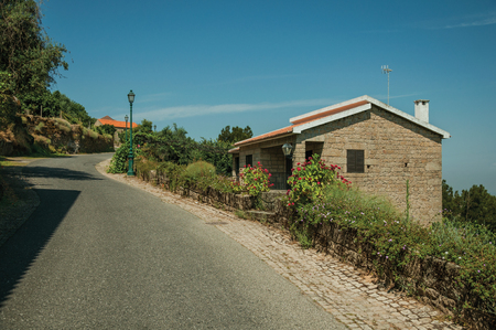 Asphalt road on slope with stone parapet and rustic house, on hilly landscape covered by trees in a sunny day at Monsanto. Considered one of the cutest and most peculiar historic village of Portugal.のeditorial素材