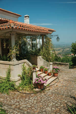 Charming old house facade with stairs leading to porch full of flowers, on hilly landscape in a sunny day at Monsanto. Considered one of the cutest and most peculiar historic village of Portugal.のeditorial素材