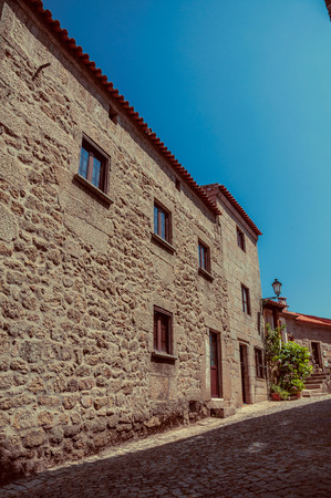 Charming facade of old stone house and flowered bushes on deserted alley, in a sunny day at Monsanto. Considered one of the cutest and most peculiar historic village of Portugal. Vintage filter.の写真素材