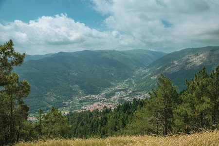 Green wooded valley with the roofs of a small village underneath, in a sunny day at the highlands of...