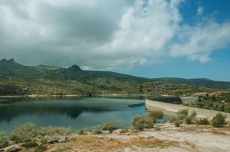 Rocky shore with bushes next to the concrete dam of Rossim Lake, in a sunny day at the highlands of Serra da Estrela. The highest mountain range in continental Portugal, with astonishing scenery.の写真素材