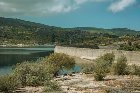 Rocky shore with bushes next to the concrete dam of Rossim Lake, in a sunny day at the highlands of...