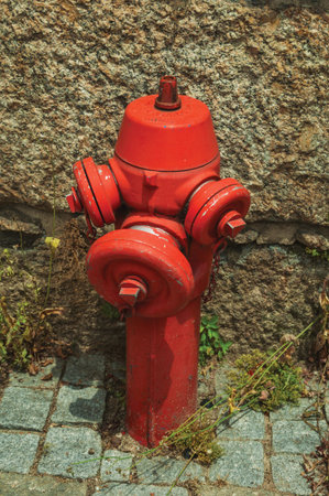 Close-up of red hydrant next to stone wall on a setts pavement at Seia. On foothill mountains, this...