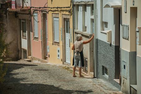 Seia, Portugal - July 19, 2018. Elder in front of colorful two-story houses on cobblestone alley at Seia. This friendly town in eastern Portugal is also known for its delicious artisanal cheese.のeditorial素材