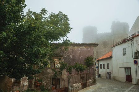 Guarda, Portugal - July 20, 2018. Cathedral behind worn old houses on alley, in the morning mist of Guarda. This friendly and well-kept medieval town is the highest in the continental Portugal.の写真素材
